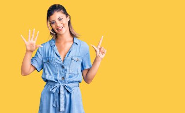 Genç ve güzel bir kadın gündelik giysiler giyer ve yedi numaralı parmaklarıyla işaret ederken kendinden emin ve mutlu bir şekilde gülümser.. 