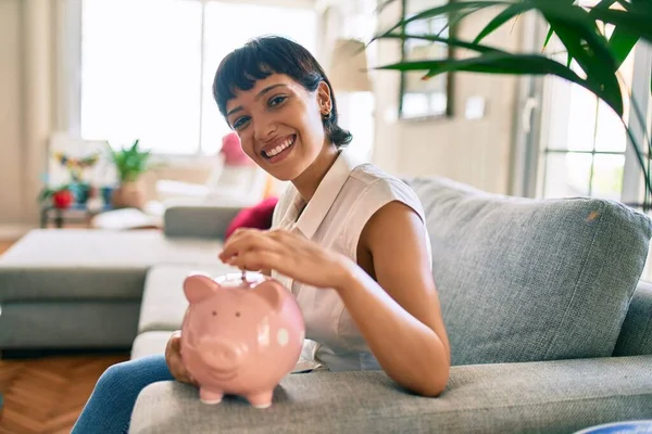 Jovem Morena Mulher Sorrindo Feliz Colocando Dinheiro Poupança Dentro Porquinho — Fotografia de Stock