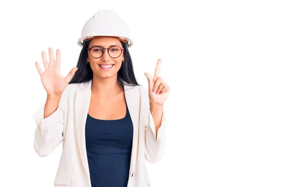 年轻美丽的拉汀姑娘戴着建筑师的硬礼帽 戴着眼镜 用七号手指显示和指尖 面带微笑 自信而快乐 — 图库照片