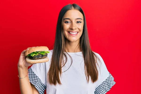 Young Hispanic Woman Eating Hamburger Looking Positive Happy Standing Smiling — Stock Photo, Image