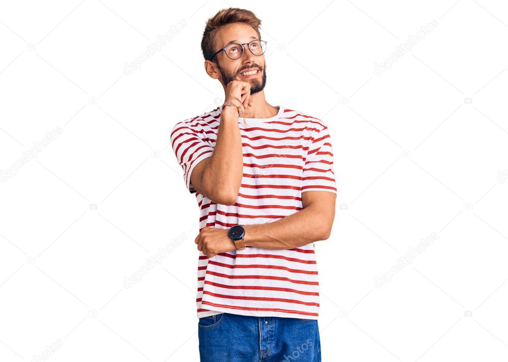 Handsome blond man with beard wearing casual clothes and glasses with hand on chin thinking about question, pensive expression. smiling and thoughtful face. doubt concept. 