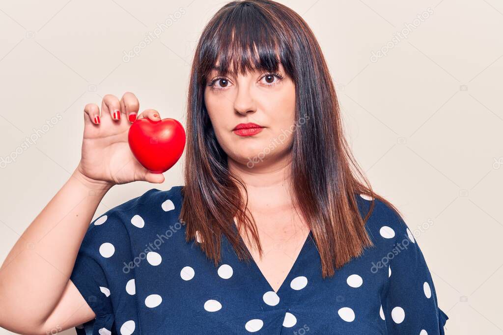 Young plus size woman holding heart thinking attitude and sober expression looking self confident 