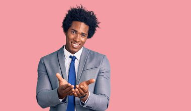 Afro saçlı, iş ceketi giymiş, elleri avuçlarında gülümseyen ve el hareketi yapan yakışıklı Afro-Amerikan bir adam. Bekleme ve koruma 