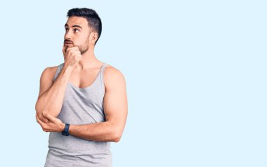 Mayolu ve kolsuz tişörtlü genç bir adam bir soru hakkında endişeli ve gergin bir şekilde düşünüyor. 