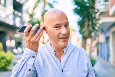 Orta yaşlı kel adam gülümsüyor. Şehirdeki akıllı telefonu kullanarak mutlu bir sesli mesaj dinliyor..