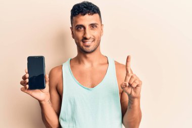 Genç İspanyol adam elinde akıllı telefonla ekranda gülümseyen bir fikir ya da soruyla mutlu bir yüzle işaret ediyor. 