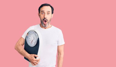 Orta yaşlı yakışıklı adam elinde tartı makinesi tutuyor. Korkmuş ve şaşırmış bir halde ağzı açık, şaşırmış bir halde. 