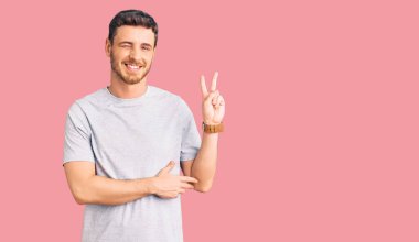 Gündelik tişört giyen yakışıklı genç adam kameraya bakıp gülümseyen ve zafer işareti yapan. İki numara.. 