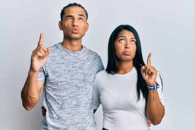 Gündelik kıyafetler giyen genç Latin çift üzgün ve üzgün görünüyor, parmaklarıyla yön gösteriyor, mutsuz ve depresif.. 