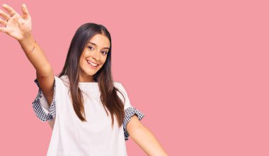 Gündelik giysiler giymiş genç İspanyol kadın kameraya bakıp sarılmak için kollarını açmış gülümsüyor. Mutluluğu kucaklayan neşeli bir ifade.. 