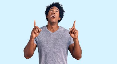 Yakışıklı Afro saçlı, sıradan giyinmiş, afili bir Amerikalı. Şaşırmış ve şaşırmış bir şekilde yukarı bakıyor, parmaklarıyla işaret ediyor ve kolunu kaldırıyor.. 