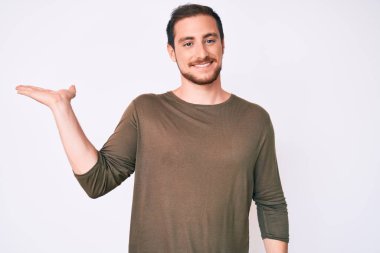 Gündelik kıyafetler giyen, neşeli gülümseyen, eli avucunda kameraya bakan genç ve yakışıklı bir adam.. 