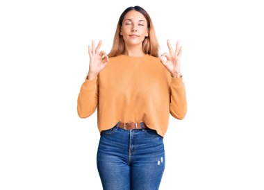 Güzel, genç bir kadın günlük kıyafetler giyiyor rahatlıyor ve gözleri kapalı gülümsüyor parmaklarıyla meditasyon hareketi yapıyor. yoga konsepti. 