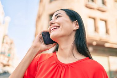 Genç Latin kız gülümsüyor. Şehirdeki akıllı telefondan konuşuyor..