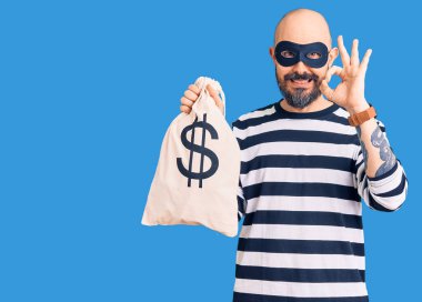 Hırsız maskesi takan genç yakışıklı bir adam. Elinde dolar sembolü olan para çantası var. Tamam işareti yapıyor. 