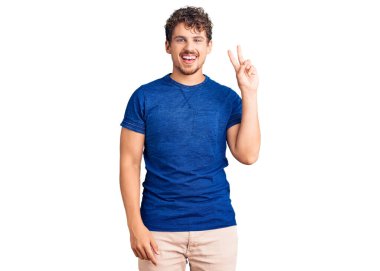 Kıvırcık saçlı, sıradan kıyafetler giyen, kameraya gülümseyen ve zafer işareti yapan genç yakışıklı bir adam. İki numara.. 