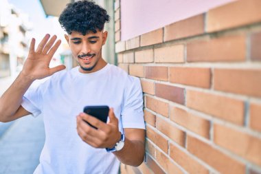 Genç Arap adam gülümseyerek şehirde akıllı telefon kullanarak video araması yapıyor..