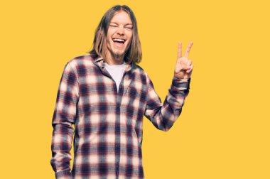 Uzun saçlı, hippi tişörtü giyen, kameraya gülümseyen ve zafer işareti yapan yakışıklı beyaz adam. İki numara.. 