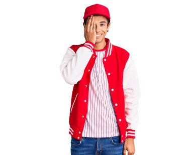 Beyzbol üniforması giyen genç Afrikalı Amerikalı bir adam bir gözünü eliyle kapatıyor, yüzünde kendine güvenen bir gülümseme ve şaşırtıcı bir duygu var.. 