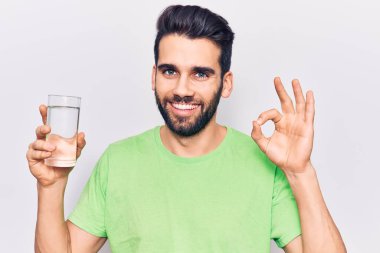 Sakallı, bir bardak su içen genç yakışıklı adam parmaklarıyla imza atıyor, gülümseyerek mükemmel bir sembol oluşturuyor. 
