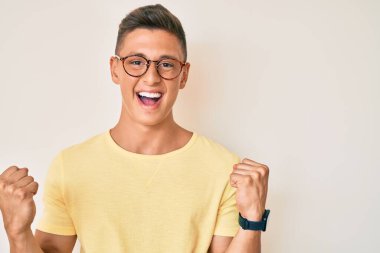 Gündelik kıyafetler ve gözlük takan genç İspanyol çocuk gururla haykırıyor, zaferi kutluyor ve başarıyı kollarını kaldırarak kutluyor. 