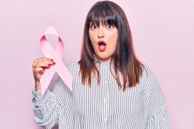 Elinde pembe kanser kurdelesi tutan genç ve iri bir kadın ağzı açık kalmış, korkmuş ve hayrete düşmüş, inançsız bir yüz. 