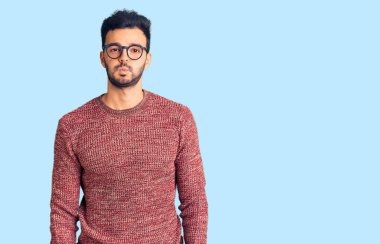 Kış süveteri giyen, gözlüklü, komik yüzlü genç, yakışıklı İspanyol adam. Havayla şişmiş ağız, çılgın bir ifade.. 