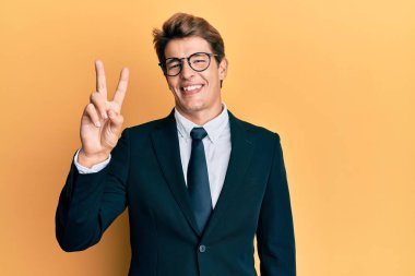 Yakışıklı, beyaz takım elbiseli ve kravatlı adam iki numaralı parmaklarıyla kendini beğenmiş ve mutlu bir şekilde iki numarayı gösteriyor.. 