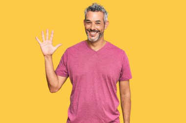 Orta yaşlı, gri saçlı, günlük kıyafetler giyen, beş numaralı parmaklarıyla işaret eden, kendinden emin ve mutlu bir adam.. 