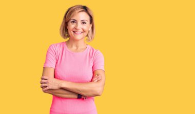 Spor kıyafetleri giyen, kollarını kavuşturup kameraya bakarken gülümseyen genç sarışın kadın. pozitif kişi. 