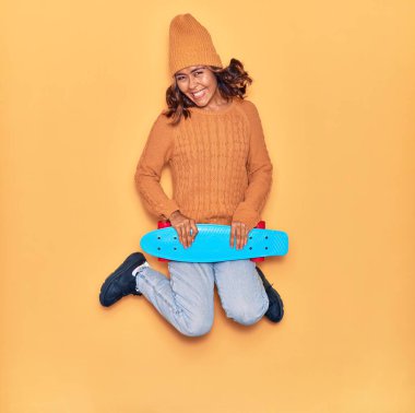 Genç, güzel Latin patenci kadın mutlu gülümsüyor. Yüzünde tebessümle, izole edilmiş sarı arka planda kayarak zıplıyor.