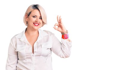 Genç sarışın, iri yarı, rahat tişört giyen, gülümseyen, el ve parmaklarıyla 