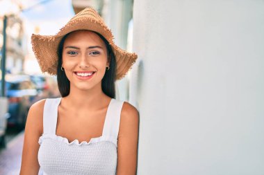 Genç Latin kız yaz stili giyiniyor ve gülümsüyor. Duvara yaslanıyor..