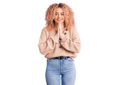 Kış kazağı giyen, kıvırcık saçlı genç sarışın kadın elleriyle dua edip af diliyor kendinden emin bir şekilde gülümsüyor.. 