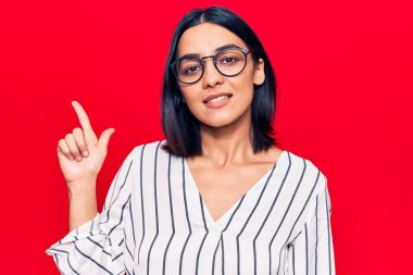 Genç ve güzel Latin kadın gündelik giysiler içinde gülümsüyor bir fikir veya soru işareti ile mutlu bir yüzle, bir numara 