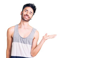 Gündelik kıyafetler giyen genç İspanyol adam neşeli bir şekilde gülümsüyor ve avuç içi kameraya bakıyor.. 
