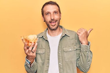 Patates cipsi tutan yakışıklı genç adam başparmağıyla yan tarafa bakıyor ve ağzı açık gülümsüyor. 