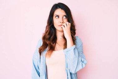Genç, güzel esmer kadın pembe arka plan üzerine gündelik giysiler giyiyordu. Elleri ağız ısıran tırnakları yüzünden gergin ve stresli görünüyordu. anksiyete. 