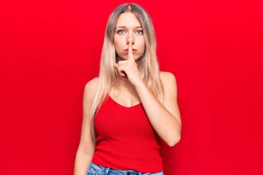 Gündelik kıyafetler giyen genç sarışın kadın parmakları dudaklarında sessiz olmak istiyor. sessizlik ve gizli konsept. 