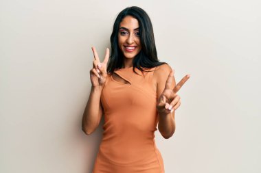 Yaz elbisesi giymiş, gülümseyen, parmaklarını zafer işareti yaparken gösteren güzel İspanyol kadın. İki numara.. 