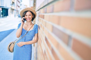 Genç ve güzel bir kız mutlu bir şekilde gülümsüyor. Akıllı telefon kullanıyor ve şehrin duvarına yaslanıyor.