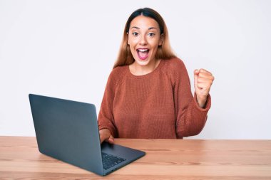 Genç esmer kadın bilgisayarda çalışırken gururla bağırıyor, zaferi kutluyor ve kollarını kaldırarak heyecanlanıyor. 