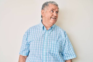 Üstün gri saçlı, günlük kıyafetler giyen, yüzünde gülümseme ve doğal ifadeyle yan yana bakan bir adam. Kendinden emin gülen. 