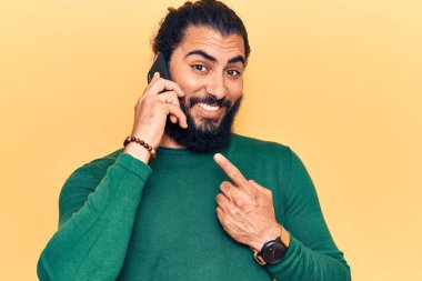 Genç Arap adam akıllı telefondan konuşuyor. Gülümsüyor, el ve parmağıyla işaret ediyor. 