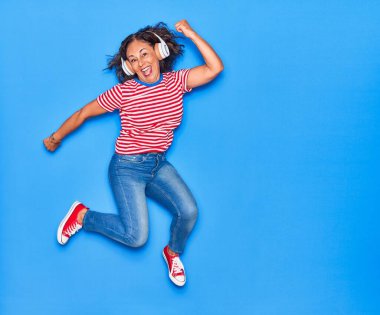 Orta yaşlı güzel İspanyol kadın mutlu gülümsüyor. Yüzünde tebessümle zıplıyor, kulaklık takıyor, müzik dinliyor.