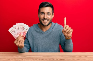 İsrail şekellerini tutan yakışıklı İspanyol bir adam bir fikirle ya da soruyla gülümsüyor ve mutlu bir yüzle işaret ediyor. 