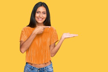 Genç esmer Arap kadın, gündelik giysiler giyip kameraya hayret ediyor ve gülümsüyor.. 