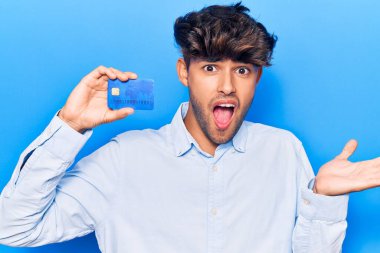 Genç İspanyol adam elinde kredi kartı tutarak başarıyı mutlu bir gülümsemeyle ve kazanan yüz ifadesiyle kutluyor. 