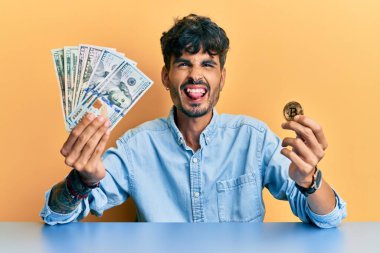Elinde dolar ve bitcoin tutan genç İspanyol adam komik bir ifadeyle mutlu bir şekilde dilini dışarı çıkarıyor.. 