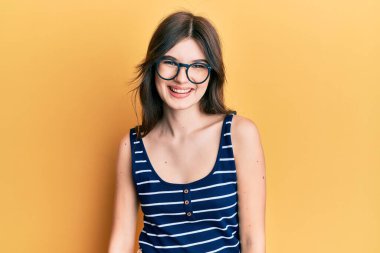 Yüzünde mutlu ve havalı bir gülümseme olan günlük kıyafetler ve gözlük takan güzel beyaz bir kız. şanslı kişi. 